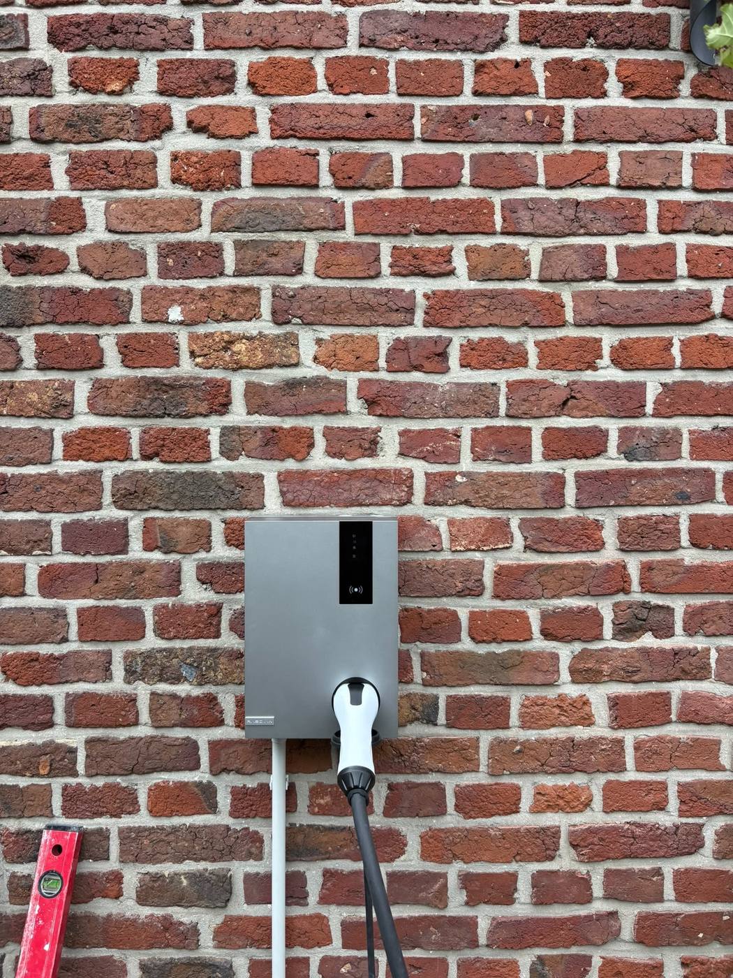 Borne de recharge installée sur le mur de façade, câble de charge branché